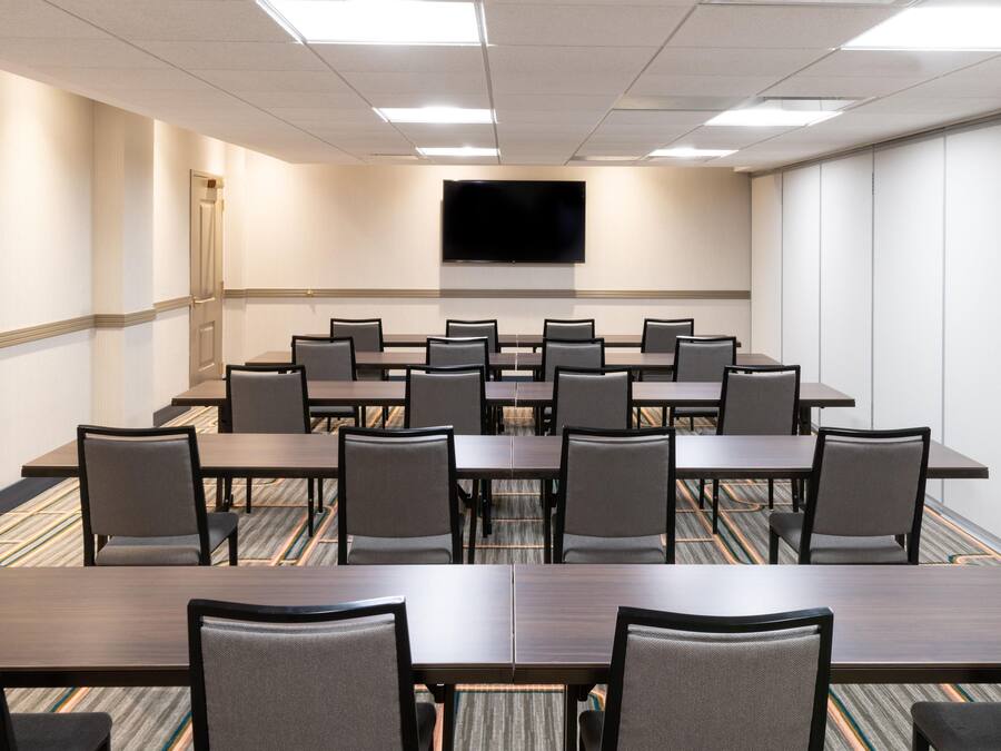 Une salle de conférence avec une longue table et des chaises, un téléviseur à écran plat fixé au mur et un revêtement de sol en moquette.