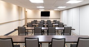 A conference room with a long table and chairs, a flat-screen TV on the wall, and carpeted flooring. - Hilton Garden Inn Flint Downtown (Flint)