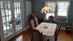 Ein Esszimmer mit einem für vier Personen gedeckten Tisch, einem Kronleuchter und einem Fenster mit Spitzenvorhängen.