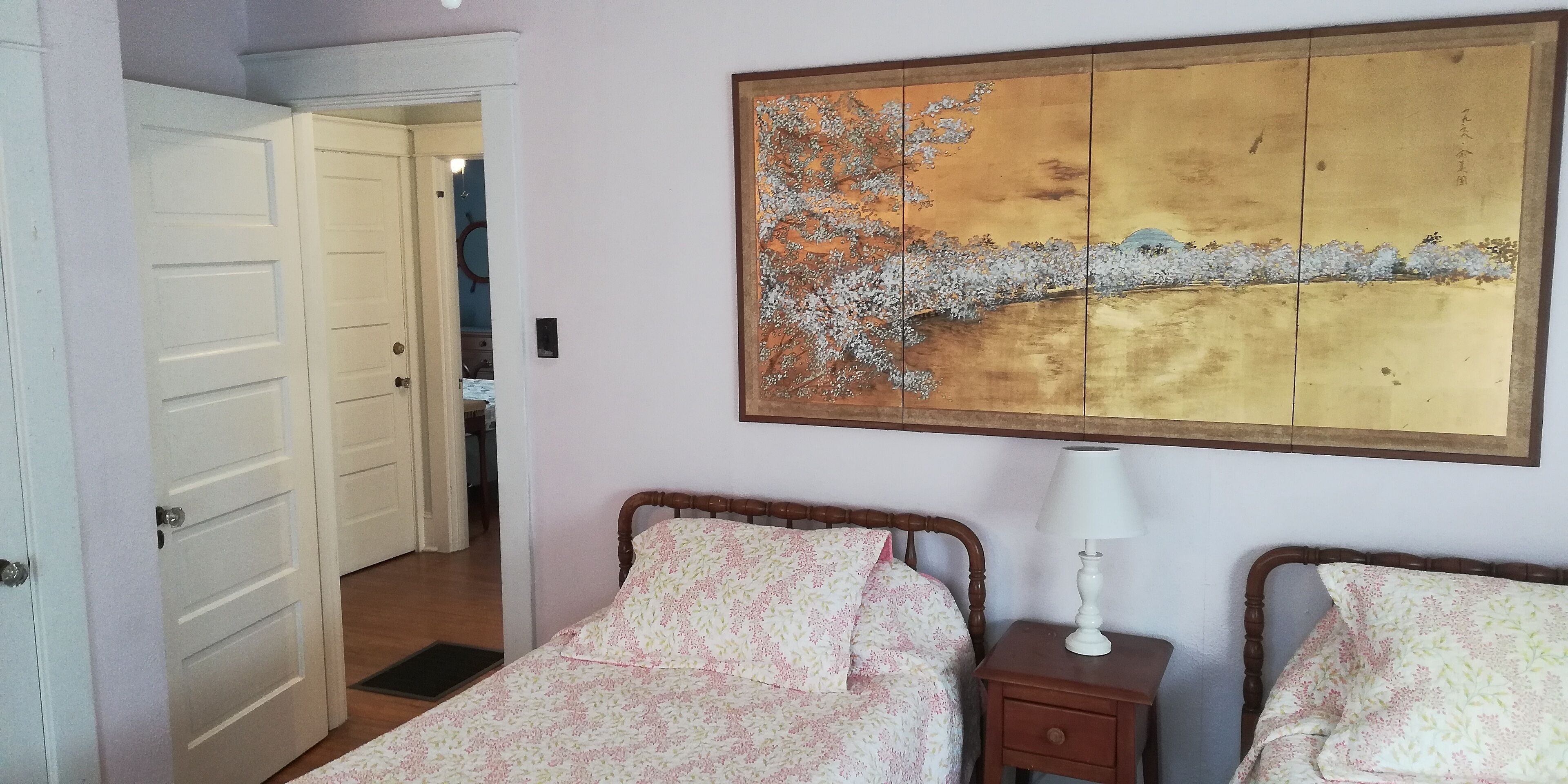 Ein Schlafzimmer mit zwei Betten, einem Holzkopfstück, einem Nachttisch mit Lampe und einem großen Gemälde an der Wand.