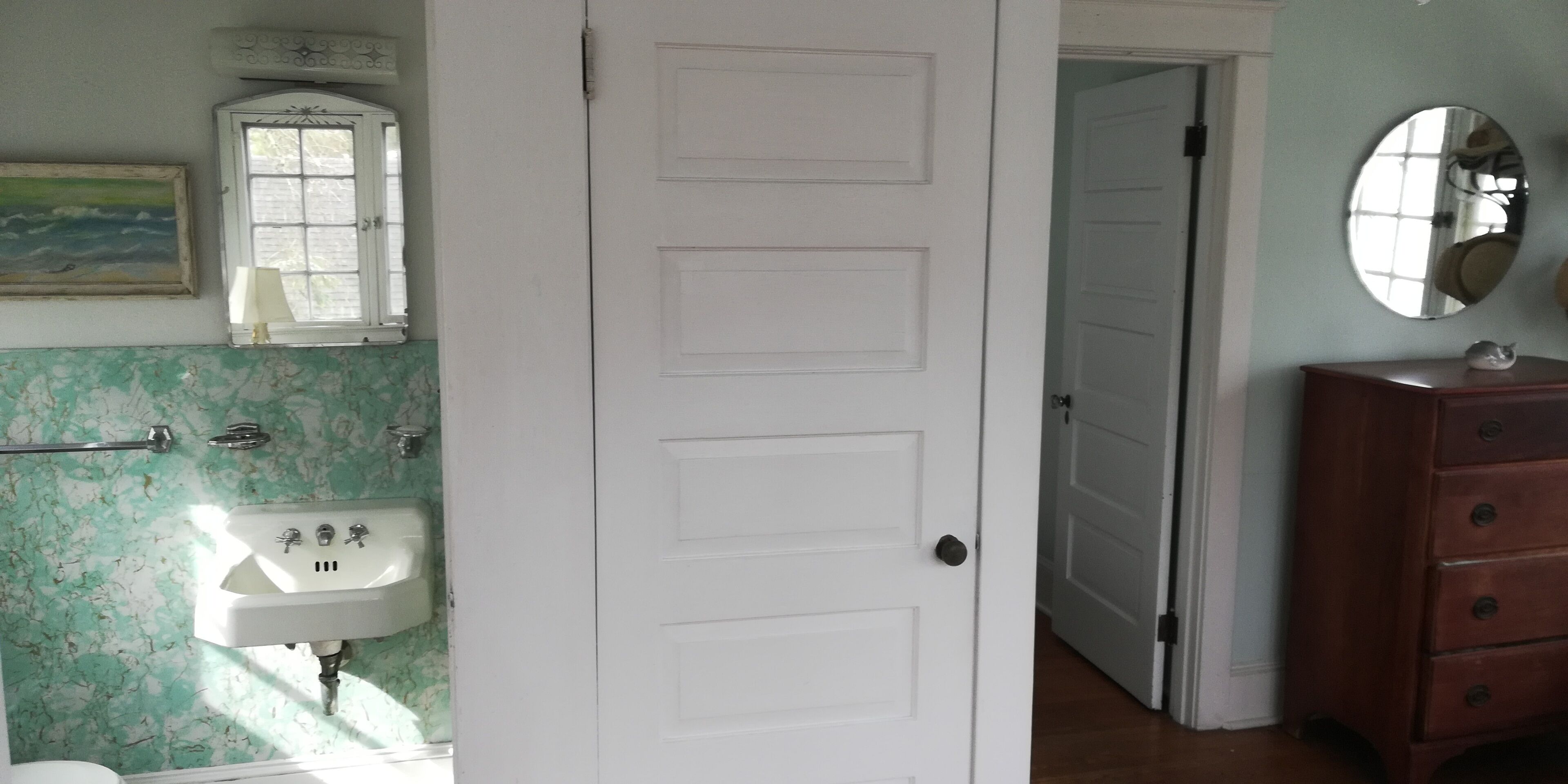 A bathroom with a white door, a sink, a mirror, and a cabinet.
