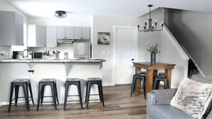 Een moderne keuken met witte kasten, een centraal eiland met barkrukken, en een eettafel met stoelen.