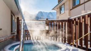 Een hottub omringd door sneeuw, met een houten omheining en bergen op de achtergrond.