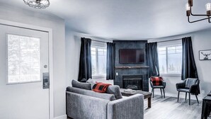 Een moderne woonkamer met een grijze bank, een open haard en een aan de muur bevestigde televisie.