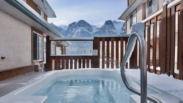 Een hottub met een houten terras en uitzicht op besneeuwde bergen.