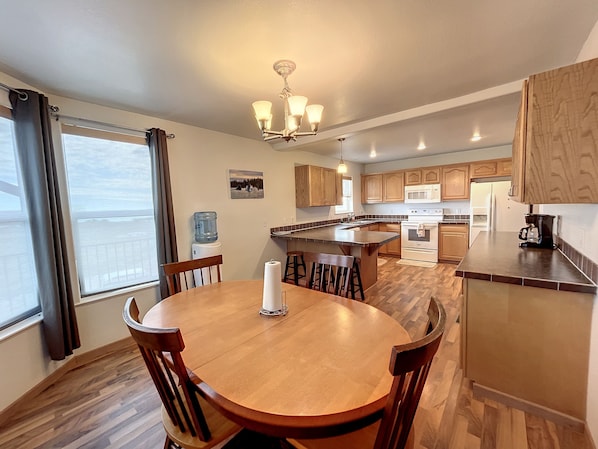 A modern kitchen with wooden cabinets, a central island, and a dining area with a round table and chairs. - The View at Lake Desmet! (Buffalo)
