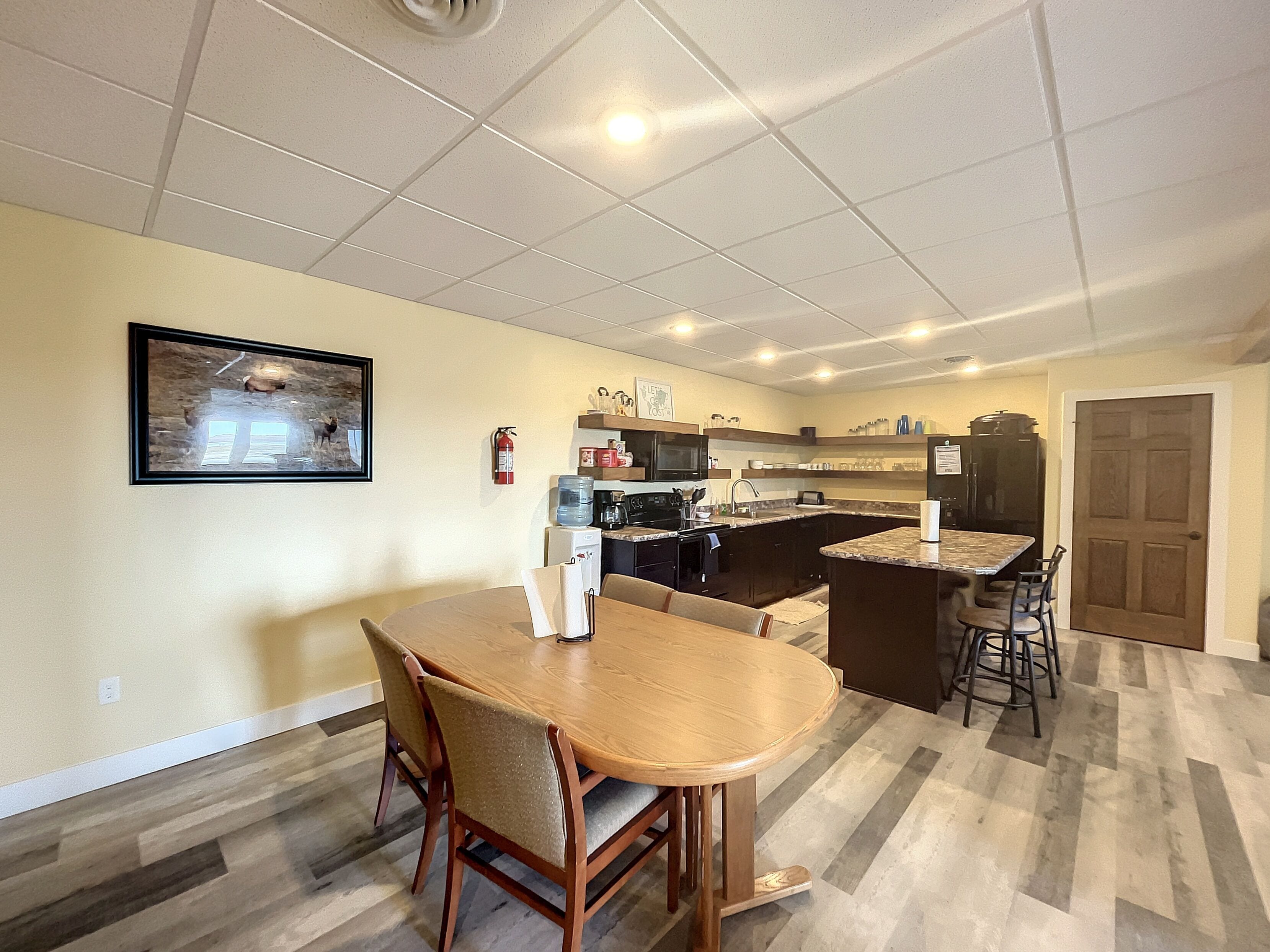 Une cuisine moderne avec des meubles de couleur sombre, un îlot central et un coin repas comprenant une table et des chaises en bois.