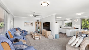 A modern living room with a sofa, TV, and kitchen area. - Duplex with views in a quiet area (Nelson Bay)