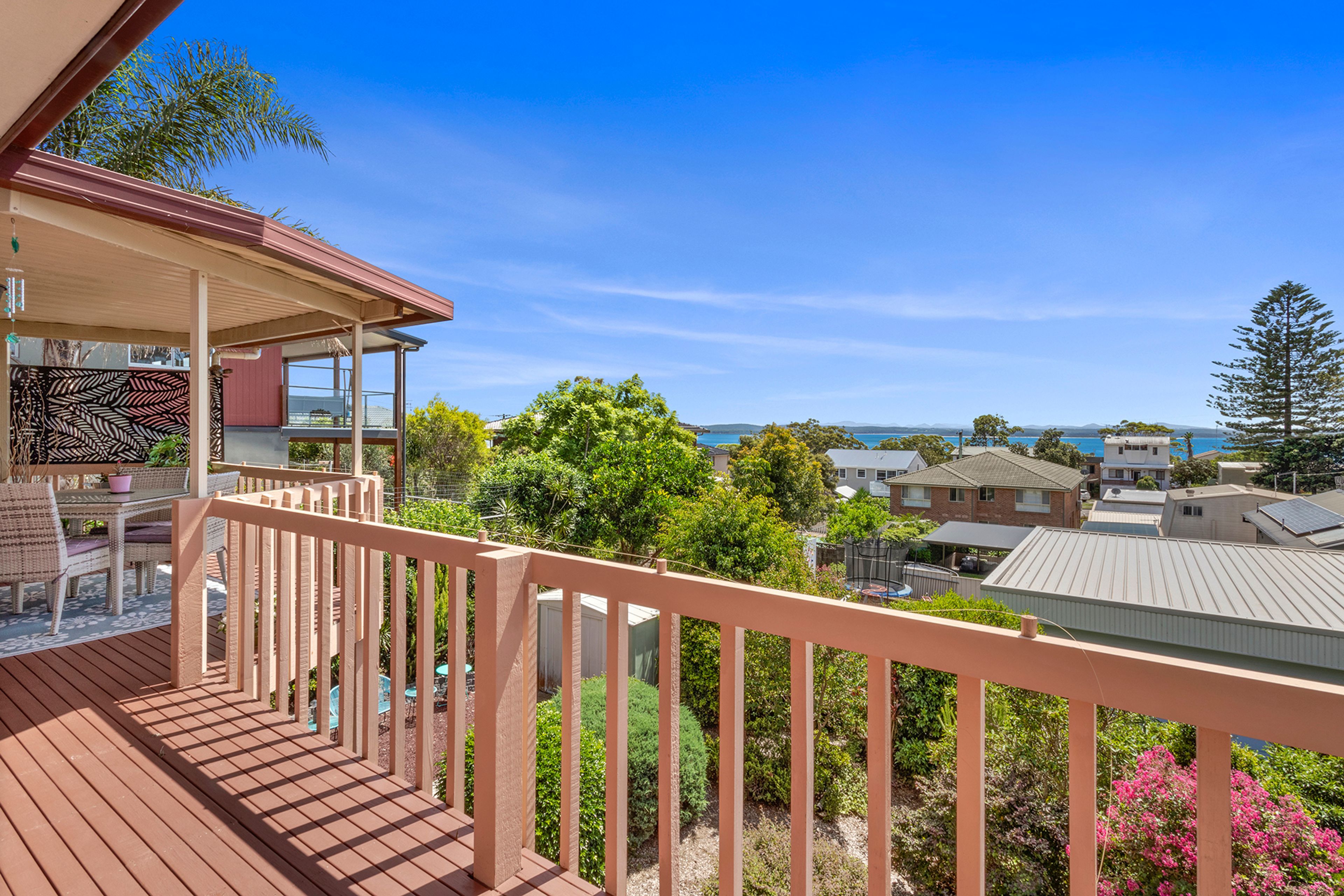 A wooden deck with a railing, overlooking a residential area with houses and a clear sky.