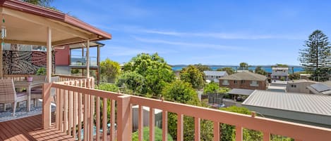 A wooden deck with a railing, overlooking a residential area with houses and a clear sky.