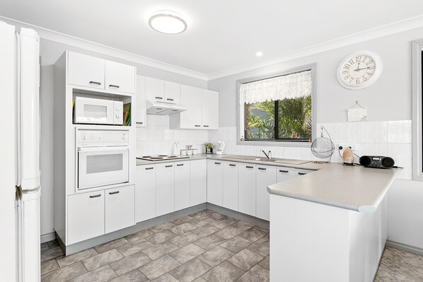 A modern kitchen with white cabinetry, a built-in oven, microwave, and a window with a view of greenery. - Wahgunyah Family Friendly in Nelson Bay (Nelson Bay)