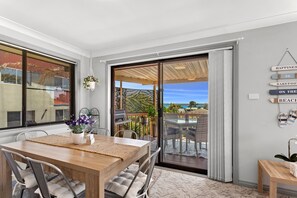 A dining area with a table and chairs, a hanging plant, and a view through a sliding glass door to an outdoor patio. - Wahgunyah Family Friendly in Nelson Bay (Nelson Bay)