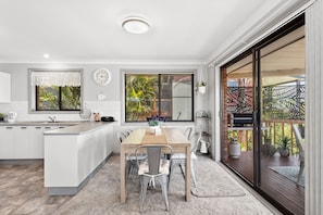 A modern kitchen with a central island, dining area with chairs, and a large sliding glass door leading to an outdoor space. - Wahgunyah Family Friendly in Nelson Bay (Nelson Bay)