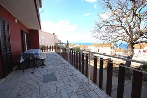 Un balcón con mesa y sillas, piso de piedra y vistas al mar y edificios.