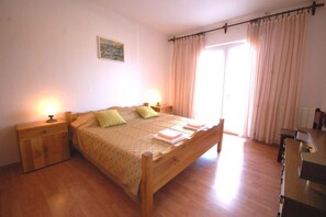 Un dormitorio con una cama de madera, dos mesitas de noche con lámparas, un aparador de madera y una ventana con cortinas.