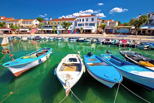A marina with several boats docked, a clear blue sky, and buildings in the background.