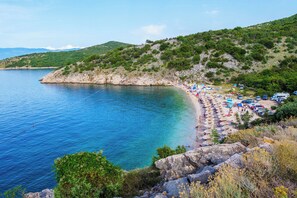 Una playa costera con aguas azul cristalina, acantilados rocosos y abundante vegetación.