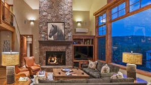 Una sala de estar acogedora con chimenea de piedra, mobiliario de cuero y un amplio ventanal con vistas panorámicas.