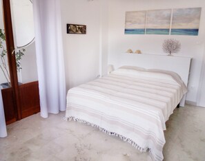 A bedroom with a bed, a painting, and a plant.