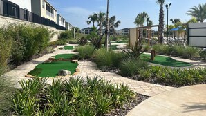 Un parcours de golf doté d’un sentier, de palmiers et d’un espace piscine avec des chaises longues.