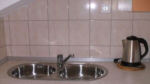 Una cocina con un lavamanos de acero inoxidable doble, una tetera sobre la encimera y paredes con azulejos color beige.