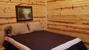Une pièce de style cabane en bois, avec un lit, des oreillers, un tableau accroché au mur et un plafond en bois.