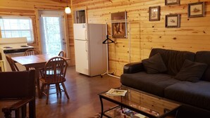 Un intérieur de chalet chaleureux comprenant un coin repas, un coin cuisine, un canapé et une étagère murale pour y poser des tableaux.