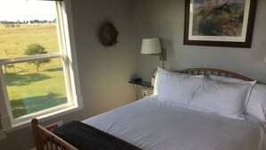 A bedroom with a large window, a wooden bed frame, white bedding, a wall-mounted lamp, and a framed picture. - Our Cozy, Quiet, Comfortable place in the Country - 2 Bedroom 900 sq ft w/view (Lockhart)