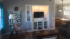 A living room with a TV, wooden furniture, a rocking chair, and a dining area with a table and chairs. - Our Cozy, Quiet, Comfortable place in the Country - 2 Bedroom 900 sq ft w/view (Lockhart)