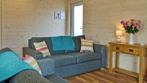 A cozy room with a grey sofa, a wooden table with a vase of flowers, and a wooden ceiling. - 2 bedroom accommodation in Burnside Park (Burnside Park)