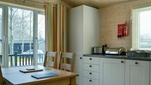 A compact kitchen with a dining area, featuring a wooden table, chairs, and a window with a view of trees and a car outside. - 2 bedroom accommodation in Burnside Park (Burnside Park)