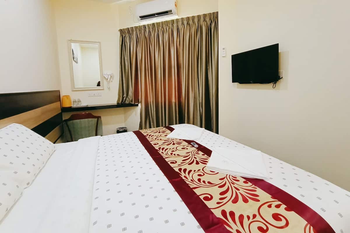 Een hotelkamer met een bed, een bureau, een stoel, een spiegel, een televisie en een raam met gordijnen.