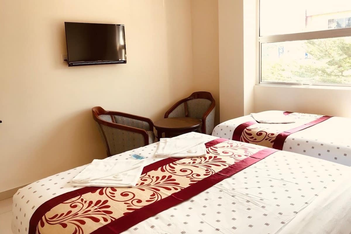 Een hotelkamer met twee bedden, een aan de muur bevestigde televisie en een raam met uitzicht op groen.