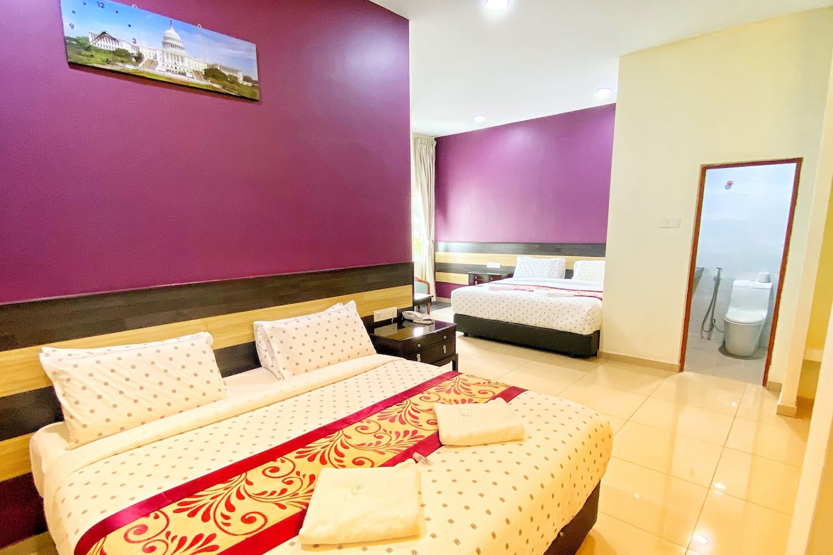Een hotelkamer met een groot bed, een kleiner bed, een badkamer en een schilderij van een gebouw aan de muur.