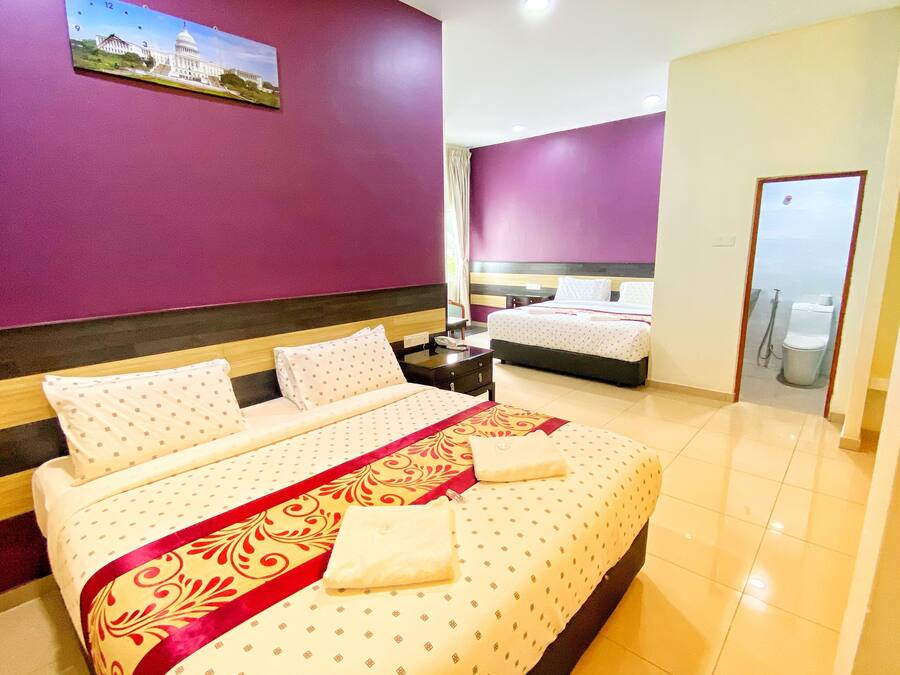 A hotel room with a large bed, a smaller bed, a bathroom, and a painting of a building on the wall.