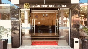 Salak Boutique -hotellin sisäänkäynti: lasiovi, tervetulomatto ja puinen vastaanottotiski.