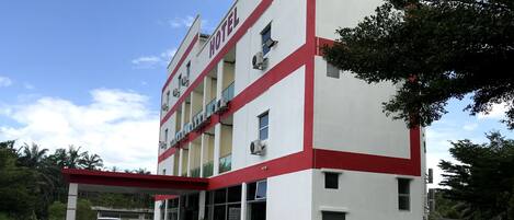 A hotel with a red and white facade, multiple floors, and a covered parking area with two cars parked.