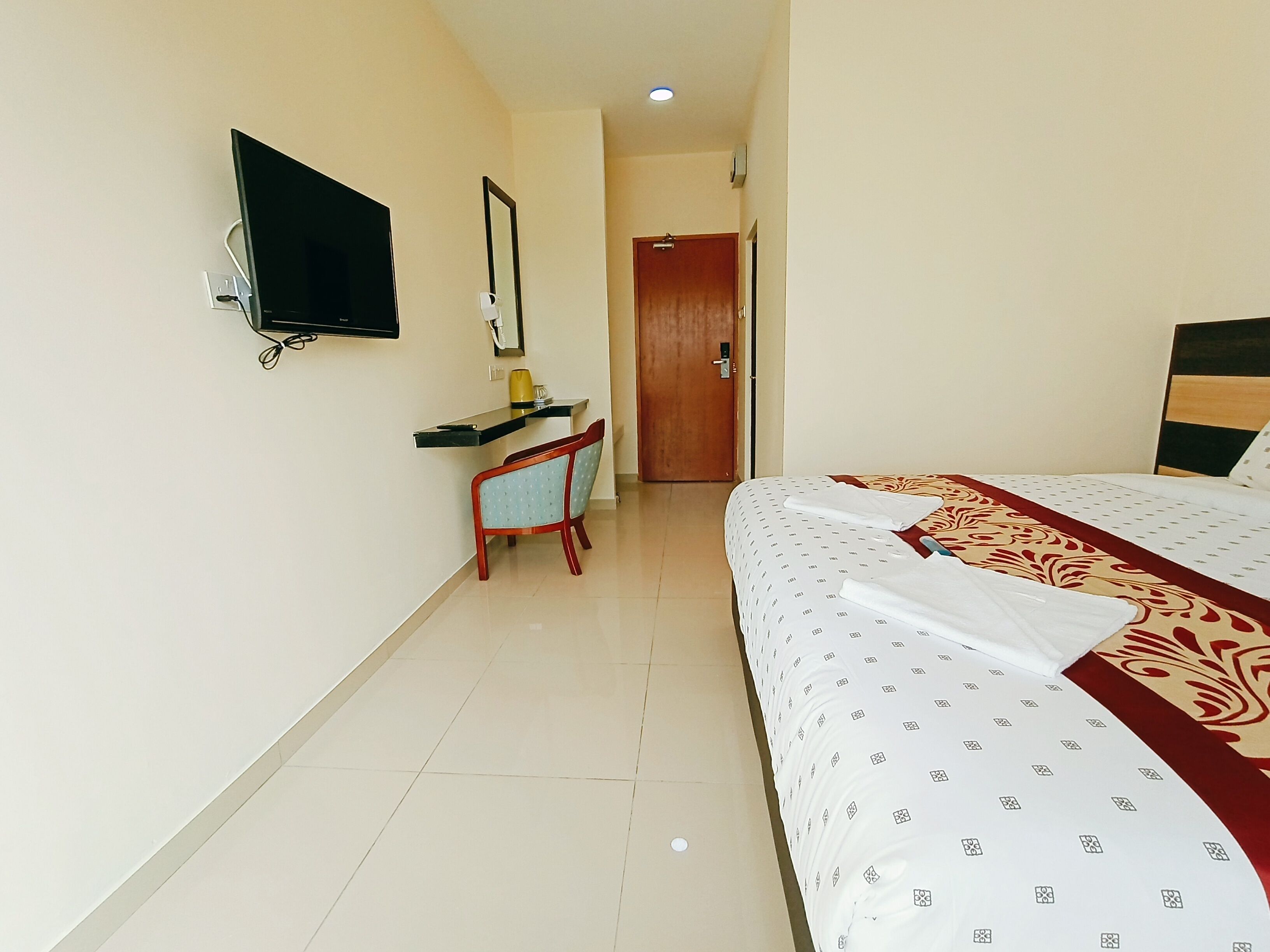 A hotel room with a bed, a desk, a chair, a TV, and a door.