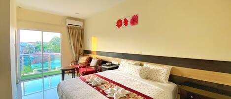 A hotel room with a large bed, a desk, a chair, a nightstand, and a view of a pool and buildings.