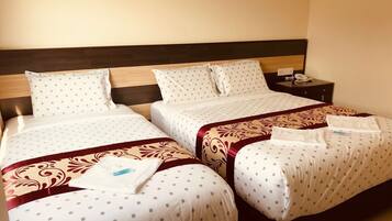 Habitación de hotel con dos camas, cada una con una colcha estampada y almohadas a juego. Hay una mesita de noche con un teléfono y un enchufe.