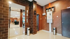 Moderni aula, jossa on tiiliseinä, vastaanottotiski ja opastekyltti, joka osoittaa wc:n sijainnin.
