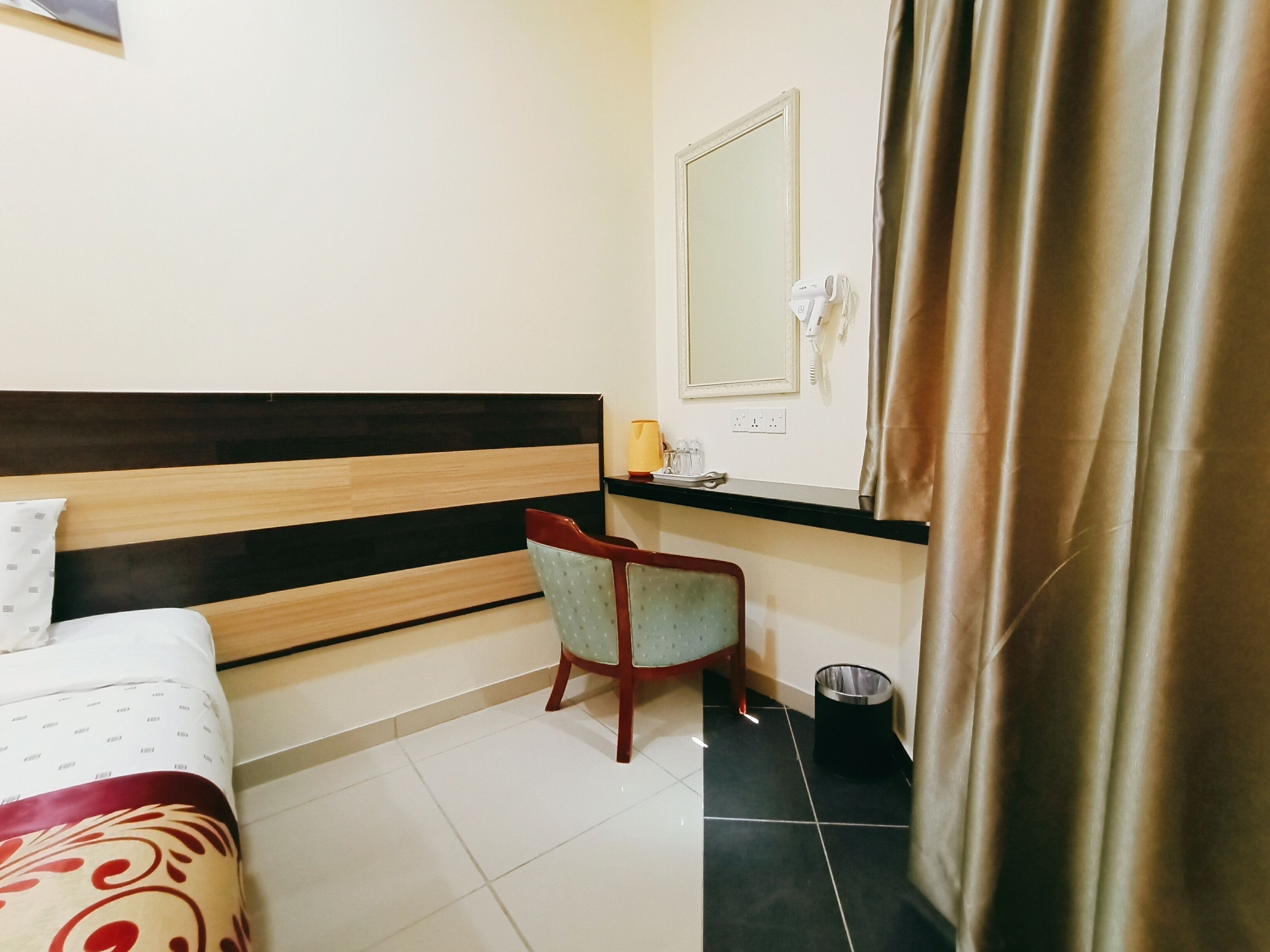 Een hotelkamer met een bed, een stoel, een klein tafeltje, een spiegel en een gordijn.