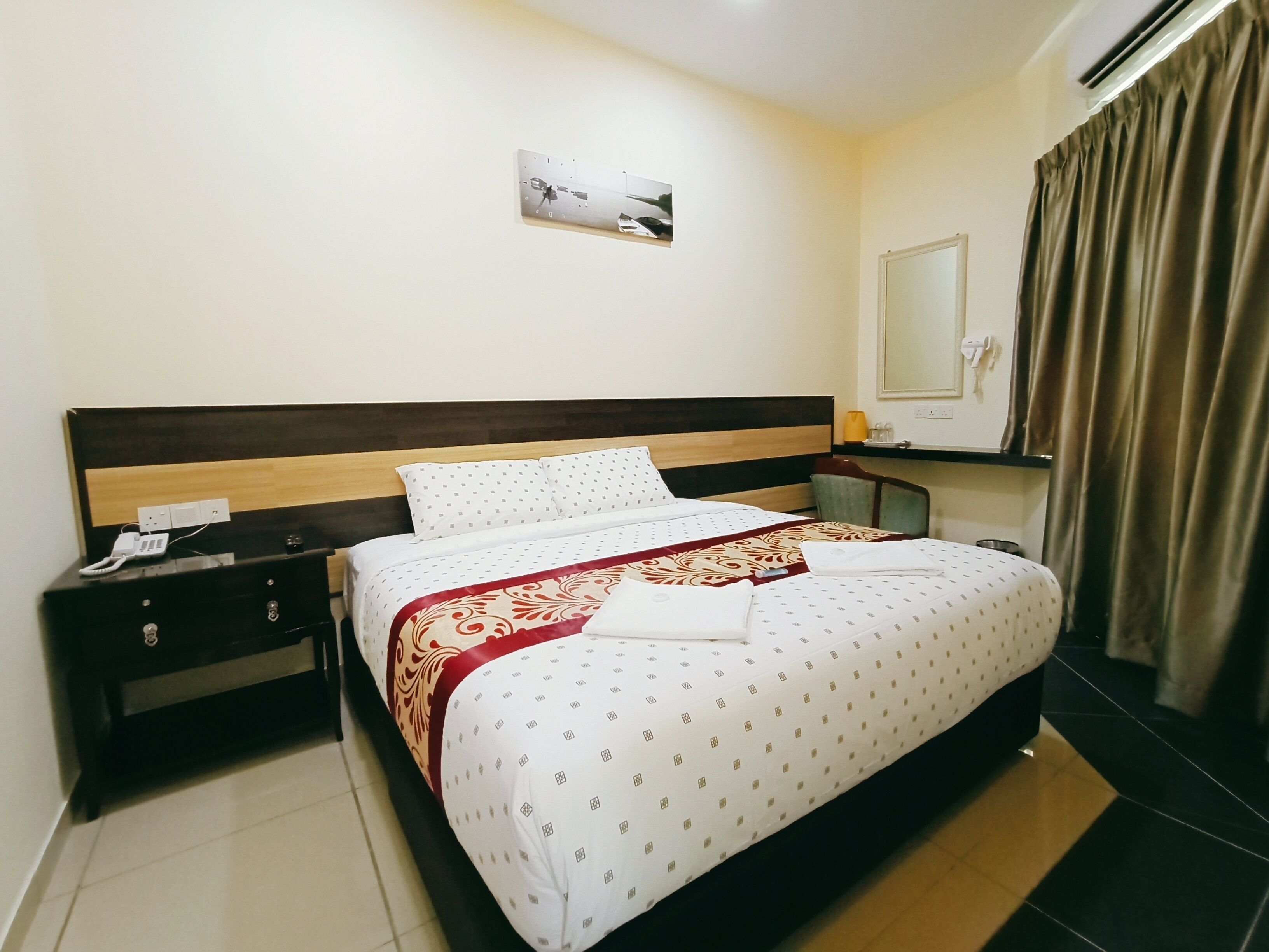 A hotel room with a bed, a nightstand, a bedside table, a mirror, and an air conditioning unit.