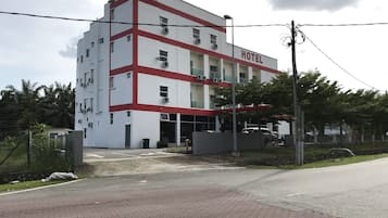 Un hotel de varios pisos con fachada roja y blanca, unidades de aire acondicionado y una entrada con portón.