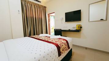 A hotel room with a bed, an air conditioning unit, a television, a mirror, and a small shelf with a kettle.