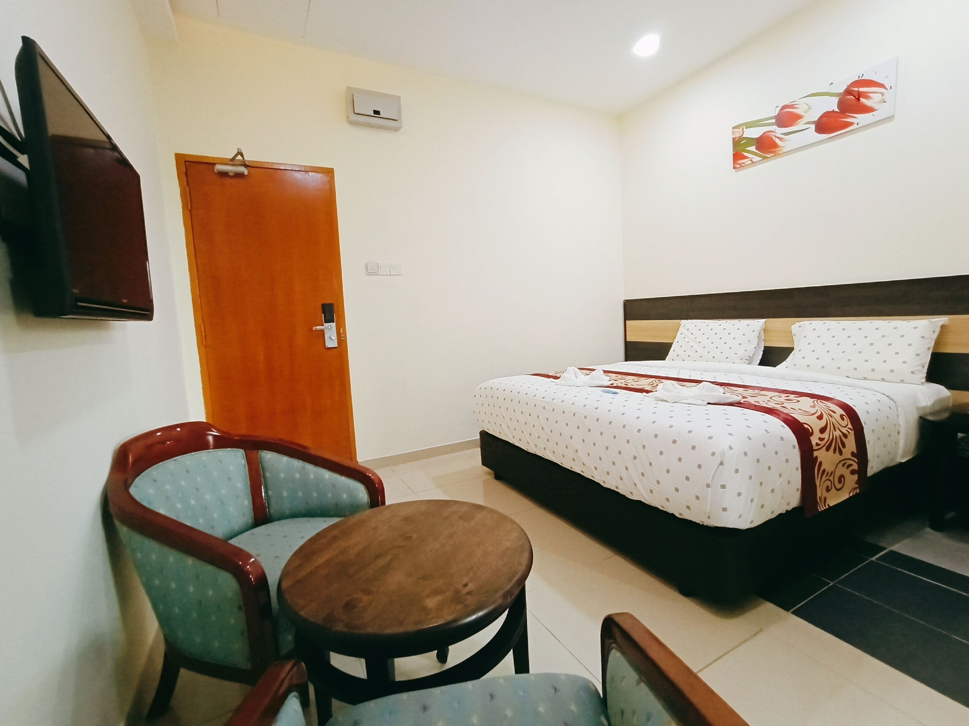 A hotel room with a bed, two chairs, a small table, a TV, and a painting on the wall.