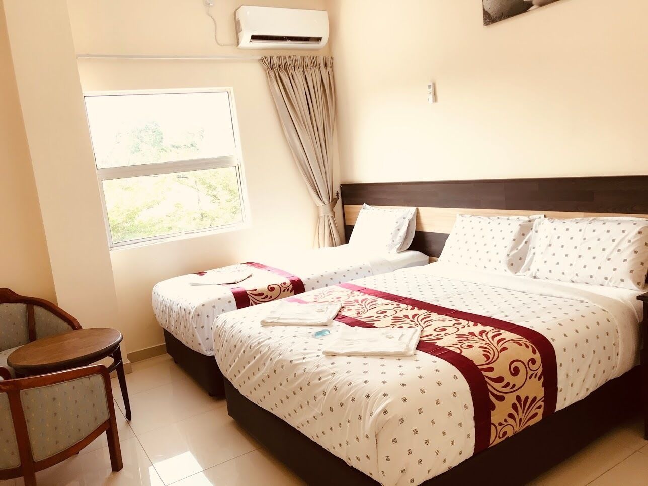Habitación de hotel con dos camas, una mesita y un ventanal con cortinas.