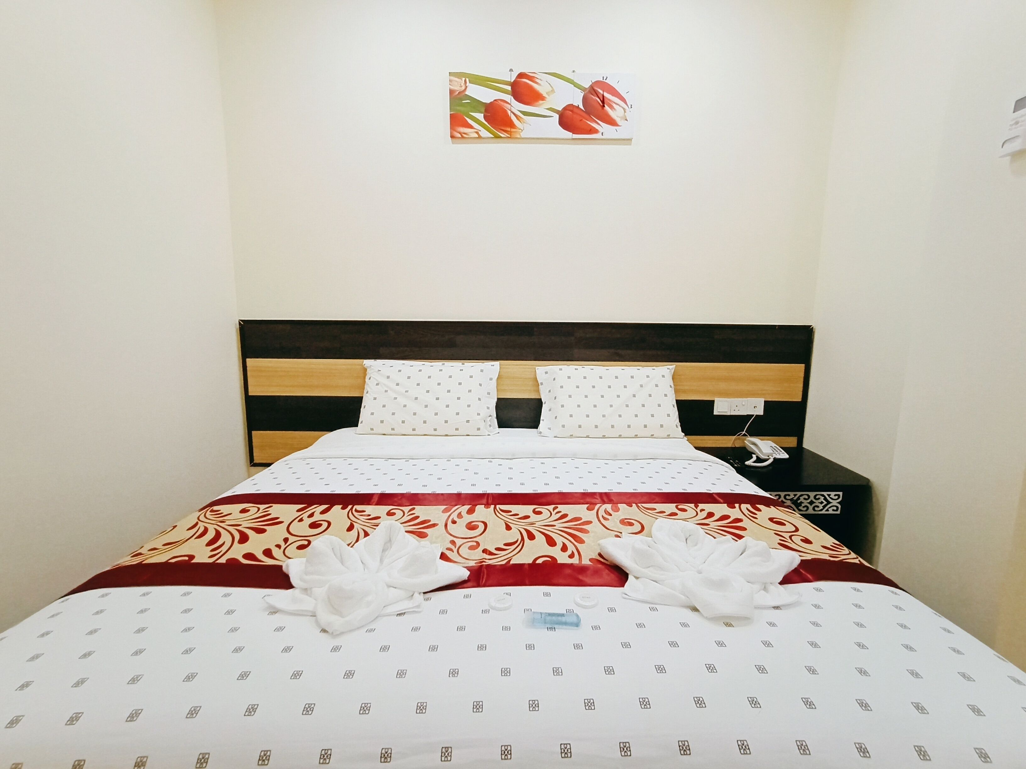 A neatly made bed with a patterned bedspread, two pillows, and a bedside table with a phone and a lamp.