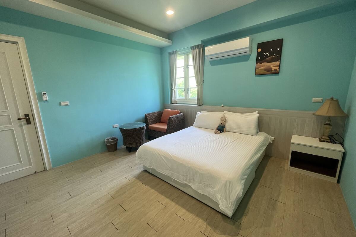 A bedroom with a bed, a chair, a lamp, and a wall-mounted air conditioner.