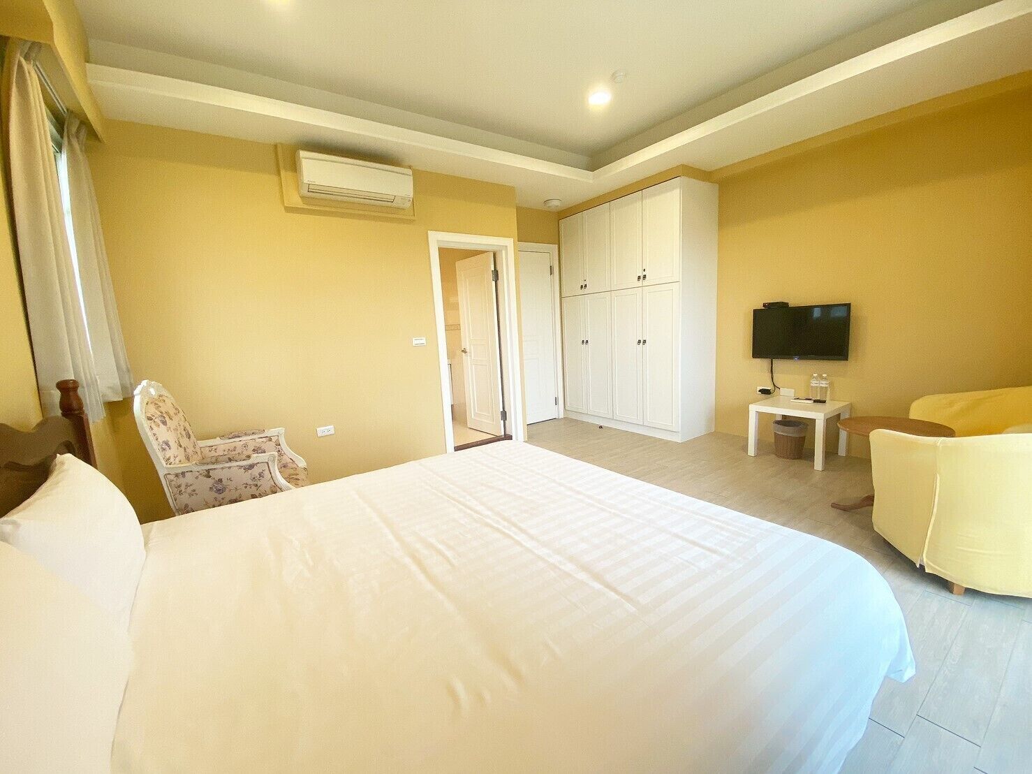 A hotel room with a large bed, a chair, a TV, and a wardrobe.
